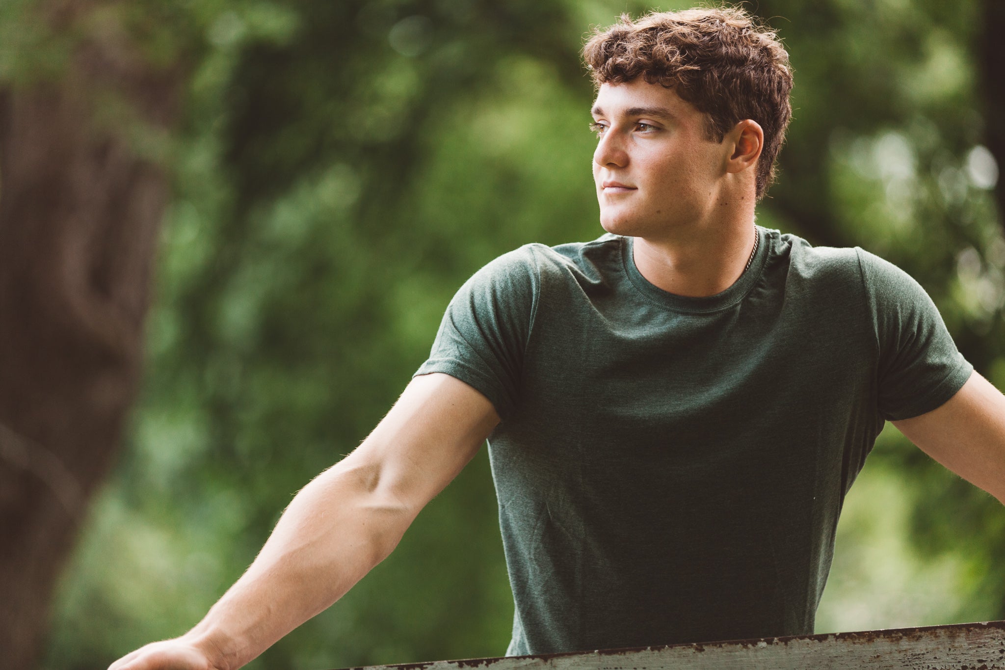 Man in a green shirt standing outdoors with trees in the background